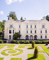 Manicured lawns and shrubbery outside of a white manor house.