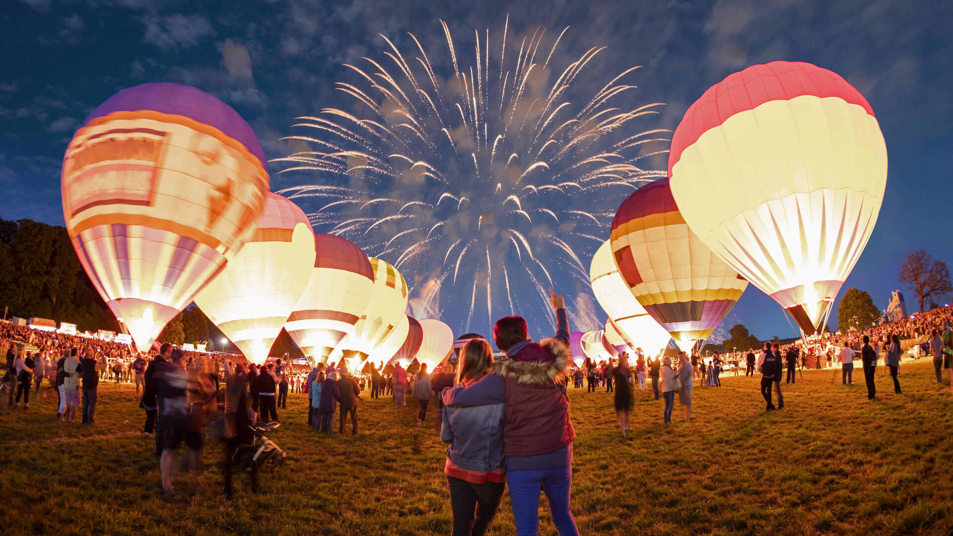 Couple watching grounded hot air balloons and fireworks in the night sky