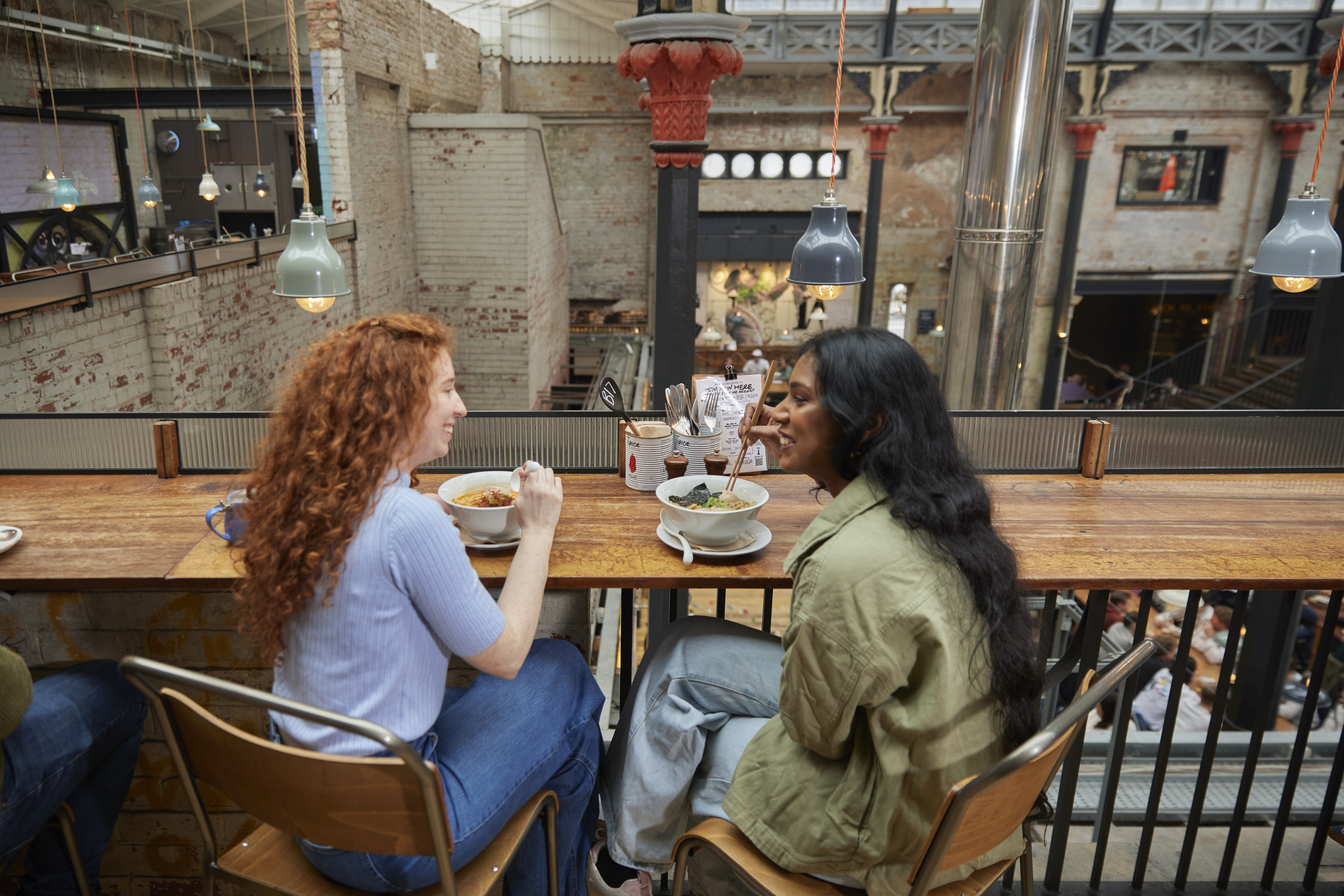 Two women enjoying lunch inside a large food hall.
