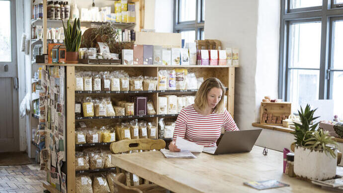 Woman in early 40s using laptop at a communal table in a health food shop and cafe