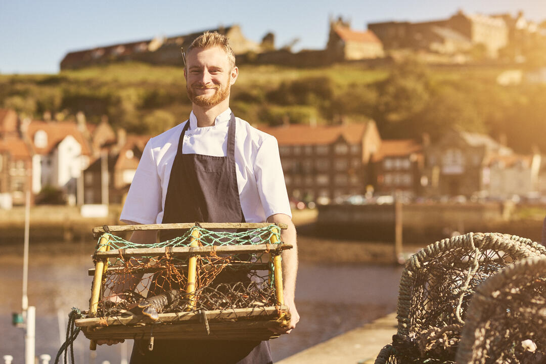 Man holding a lobster trap on a pier in the sunshine
