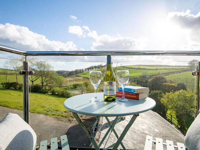 View from the balcony with a bistro table and chairs set with two novels, two wine glasses and a bottle of wine with a rural landscape in the background.
