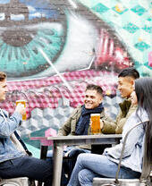 Des amis prenant un verre assis à une table en terrasse devant un graffiti coloré