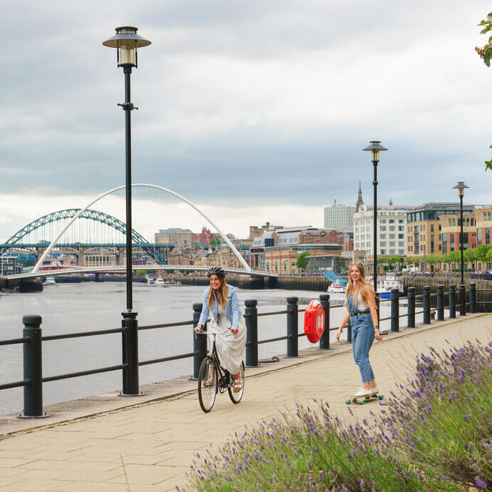 Due persone in bicicletta e skateboard su un sentiero lungo il fiume Tyne a Newcastle.