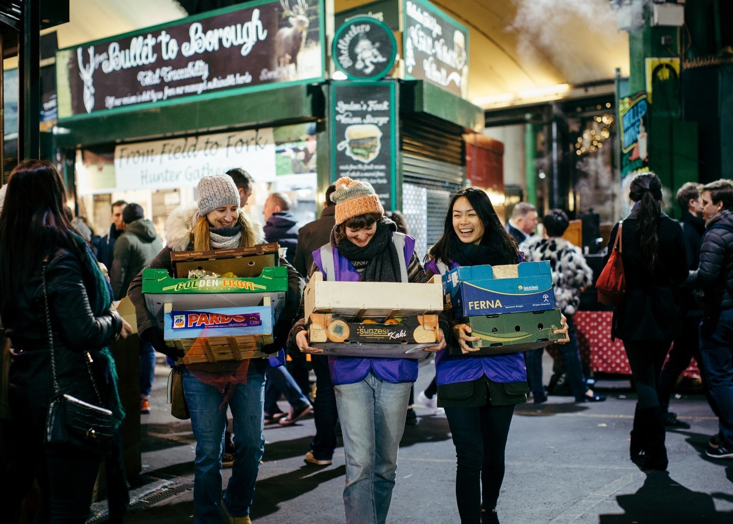Trois femmes transportant de petites caisses contenant des fruits et légumes au Borough Market