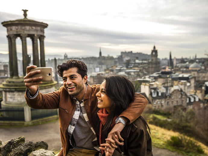 زوجان يلتقطان صورة سيلفي بهاتف محمول مع مدينة في الخلفية