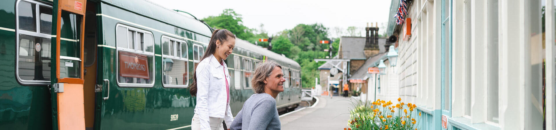 Man using a wheelchair and woman about to go into the ticket office at a station.