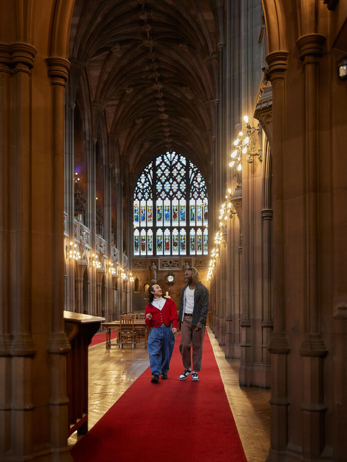 Two men chatting, exploring a large library.