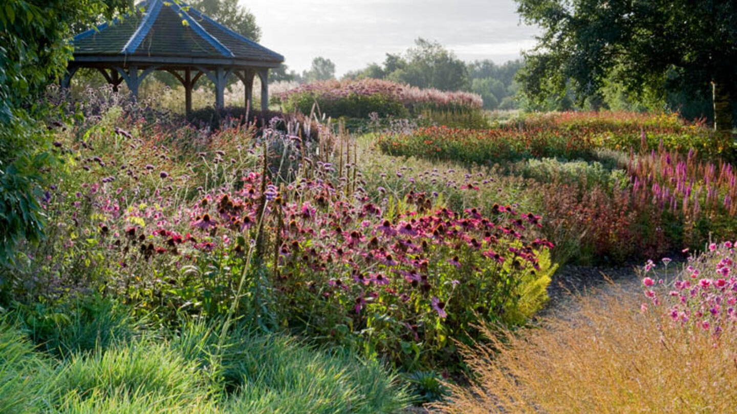 Jardín con flores coloridas y un cenador de madera al fondo.