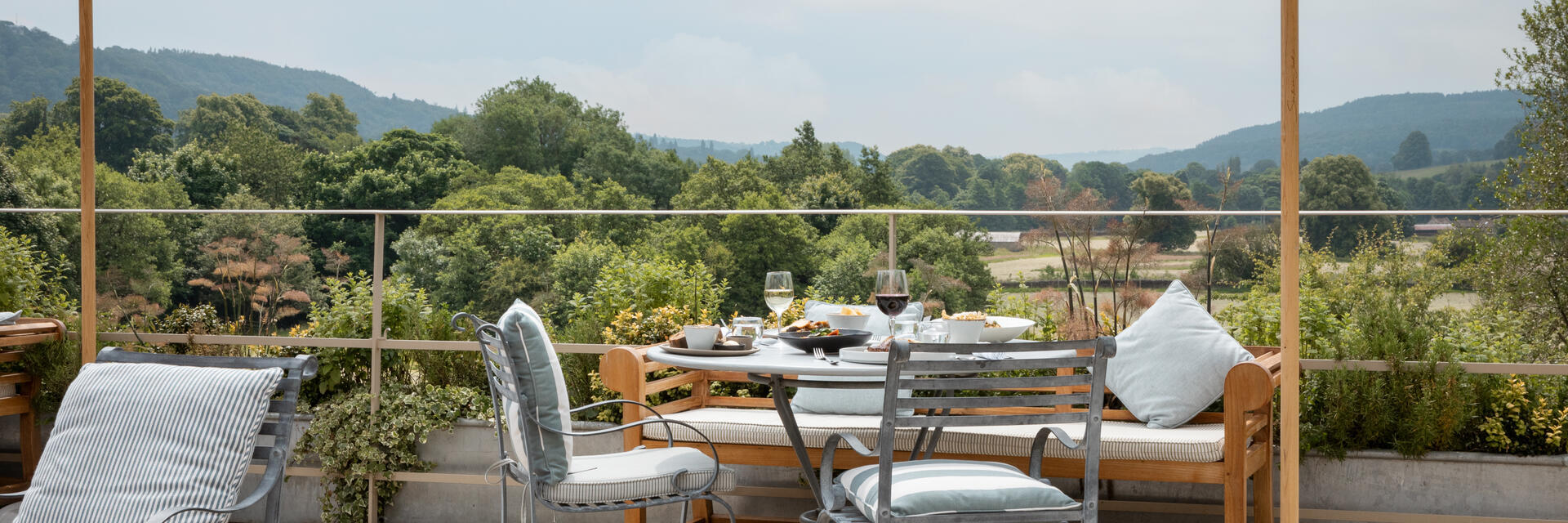 Tables on the patio with striped umbrellas overlooking the view at a luxury hotel on the grounds of a large country estate.
