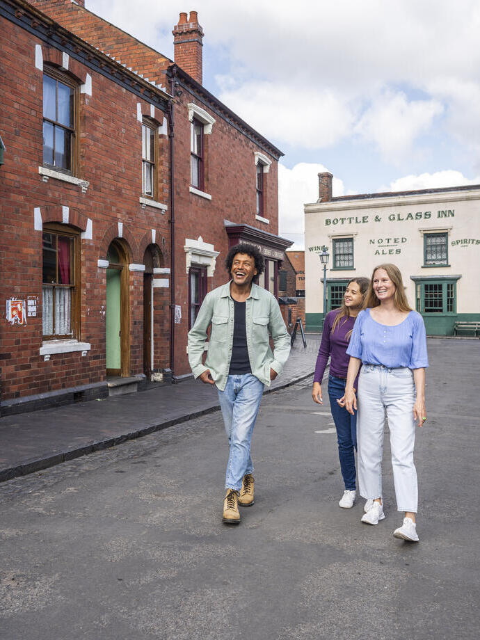 Three people walking and smiling in a historic-looking street with red brick buildings and a pub in the background.