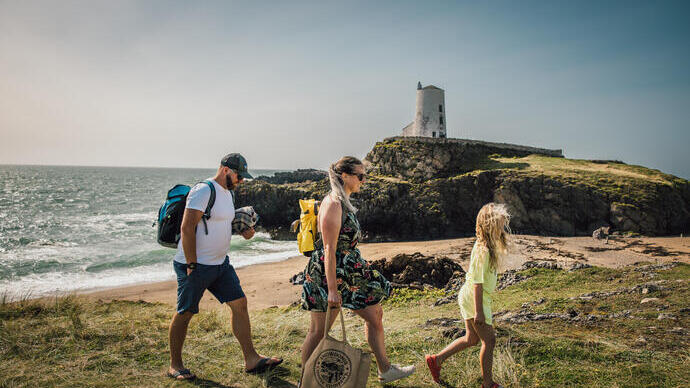 A young family walking along the beach with a lighthouse in the background.