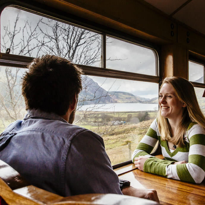 Couple sat at a table inside on a train passing through a mountainous landscape