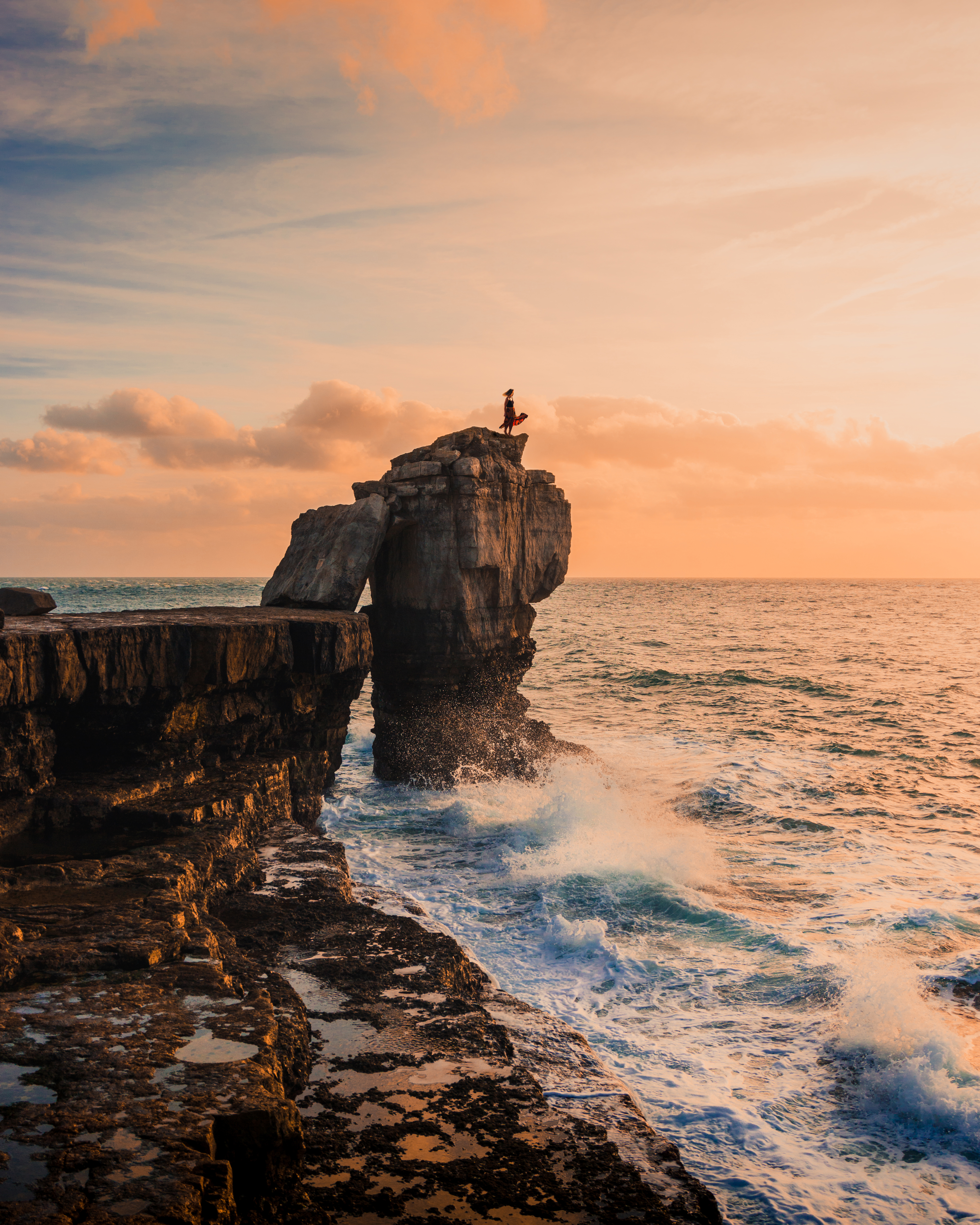 Woman standing on a rock stack looking out to sea at sunset