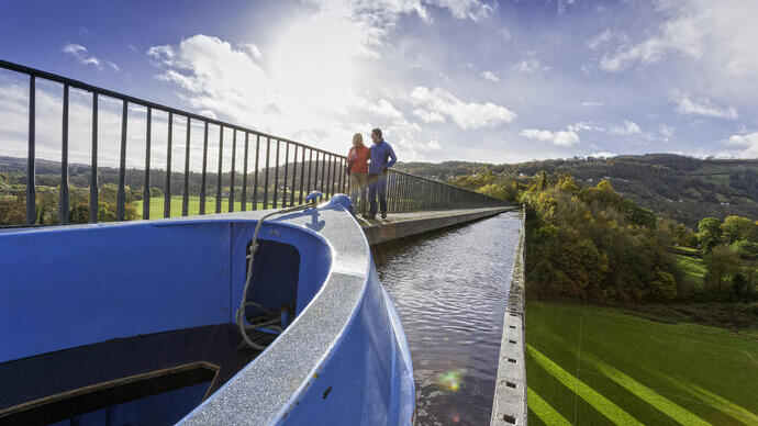 Couple walking along an Aqueduct in autumn with canal boat passing alongside.