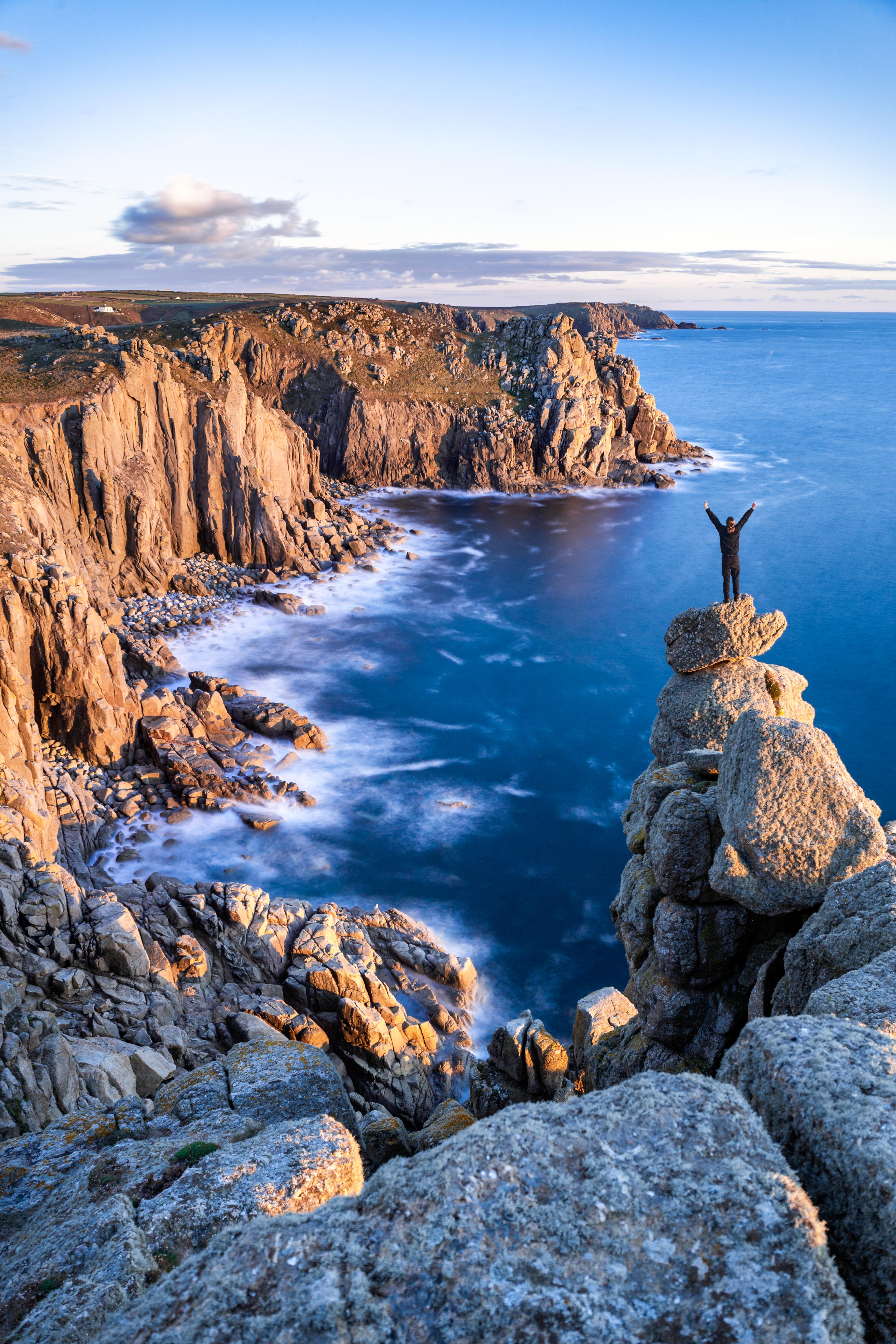 A man stands on a rocky peak looking over the rocky Cornish headland