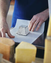 Cheese seller wrapping up goat cheese in a cheese shop.