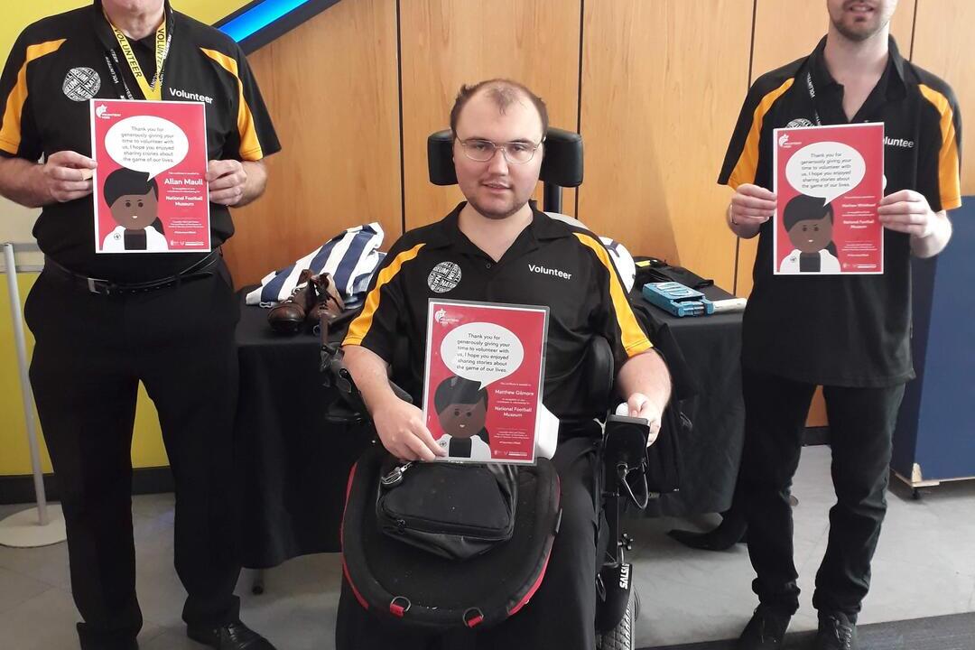 Three men posing, holding posters