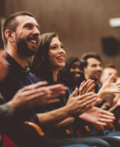 Grupo de personas sonrientes aplaudiendo en el público del teatro.
