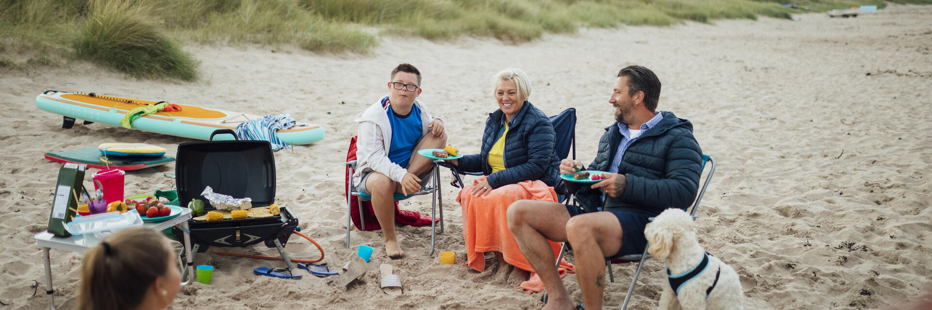 A family and their dog sat beside a picnic blanket on beach