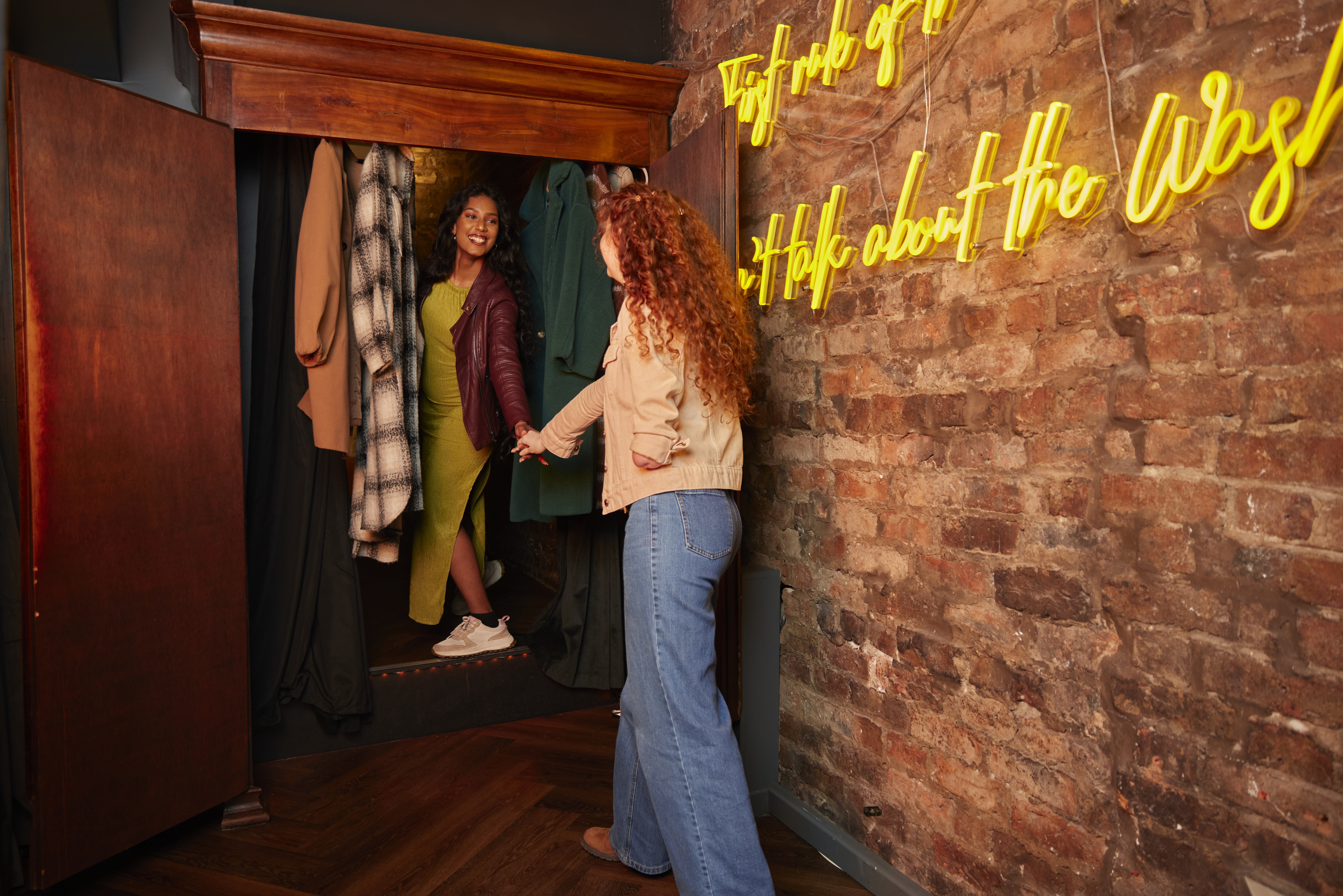 Two women entering a trendy bar through a cupboard.
