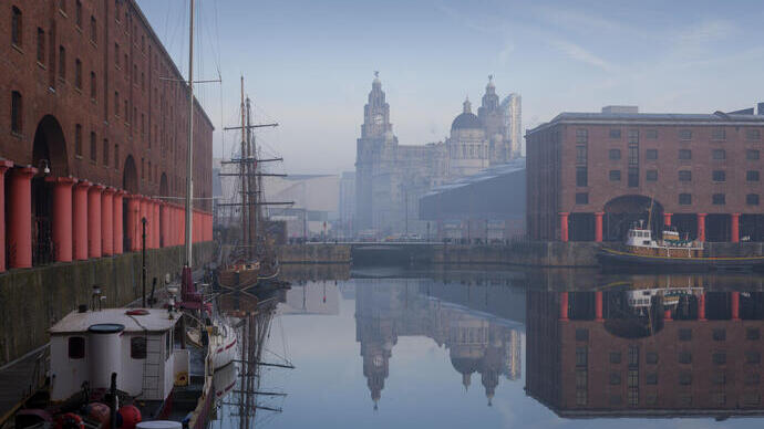 Dock with wooden ship and tall buildings on skyline.