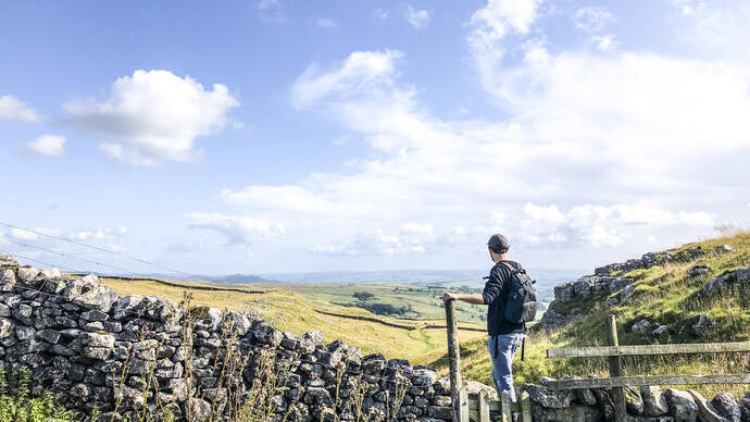 Man standing on stile over stone wall looking at landscape