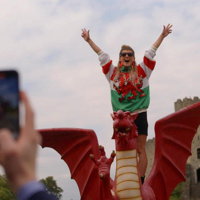 Woman standing with arms outstretched on a model Welsh dragon in front of a castle