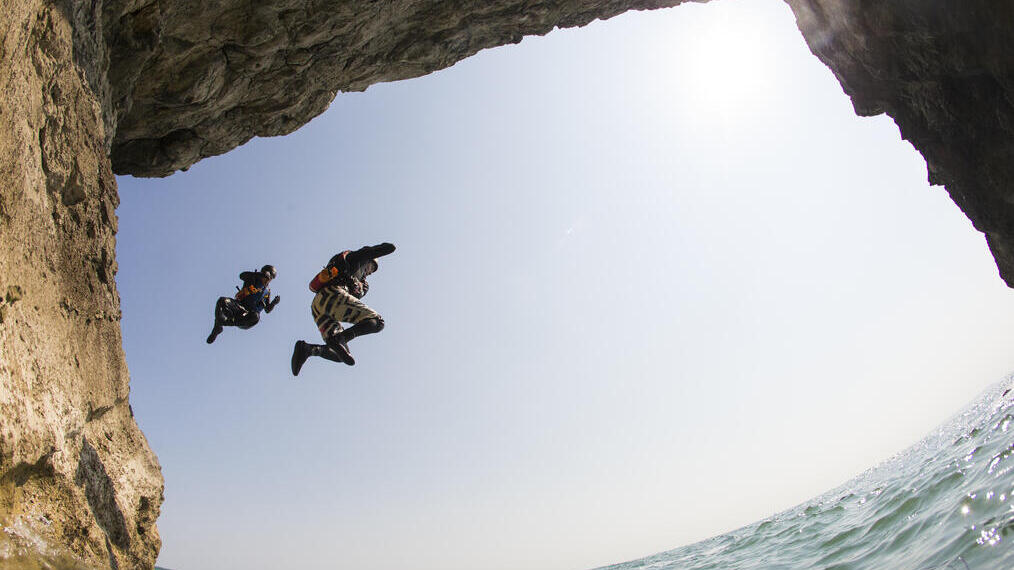 People jumping off cliff into clear blue sea