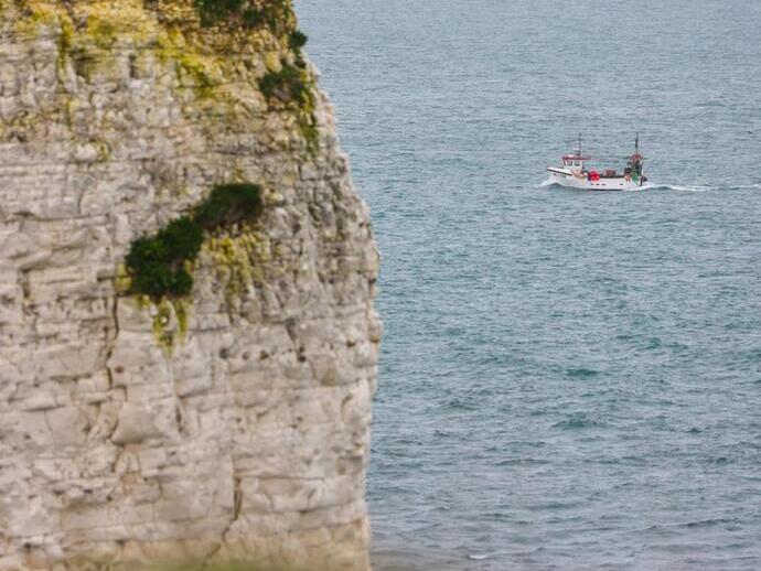 A fishing boat cruising past tall cliffs.