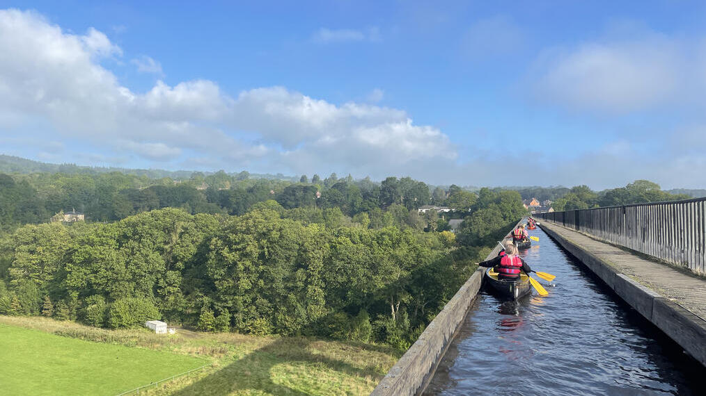 Un grupo remando en kayaks a través de un viaducto con vistas panorámicas del Parque Nacional Snowdonia/Eryri.