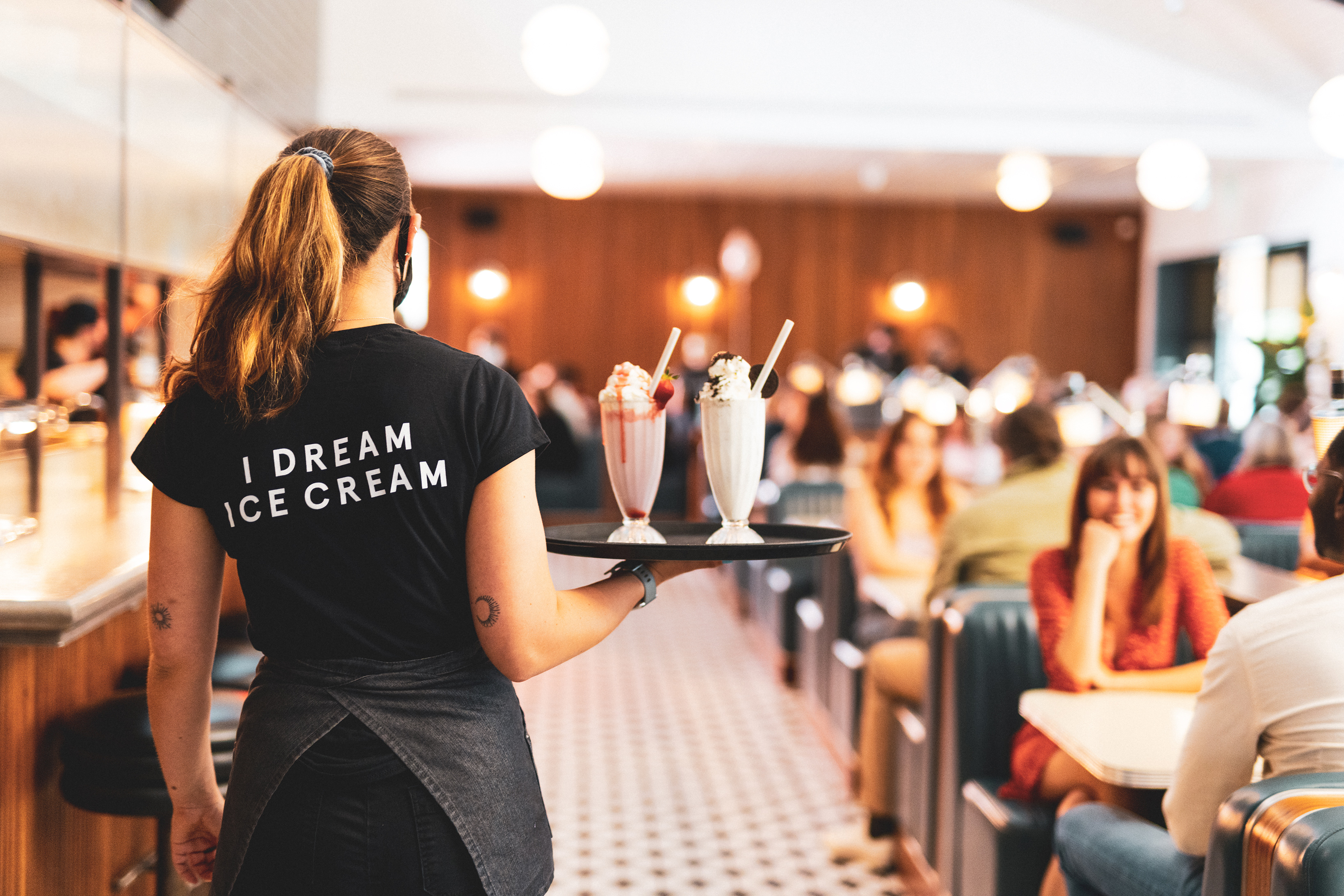 Staff member carrying two milkshakes on a tray in a diner.