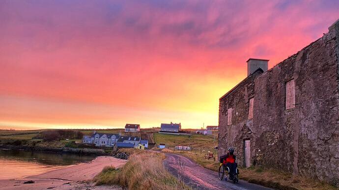 Wheelchair user going down a coastal road at sunset