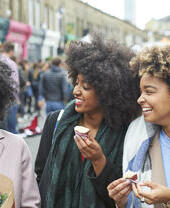 Three women laughing in a city street while eating cupcakes