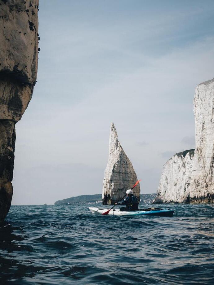 Person in canoe navigating coastline with cliffs in the background