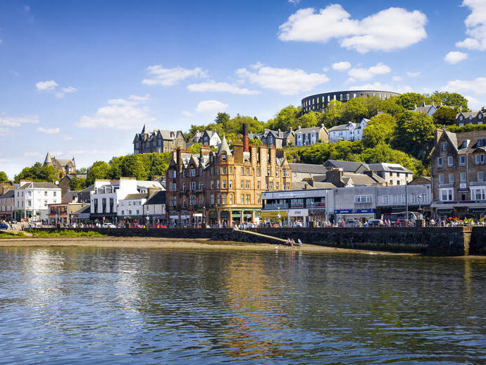 A quaint seaside village and its harbour on a sunny day with a tower on a hill in the background
