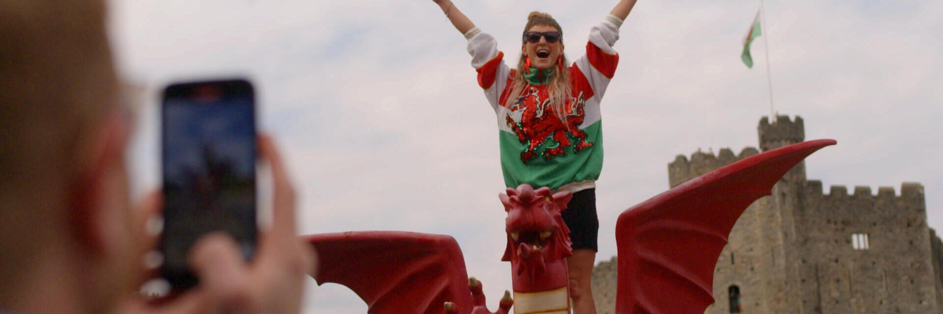 Donna in piedi con le braccia aperte su un modello di drago gallese davanti a un castello