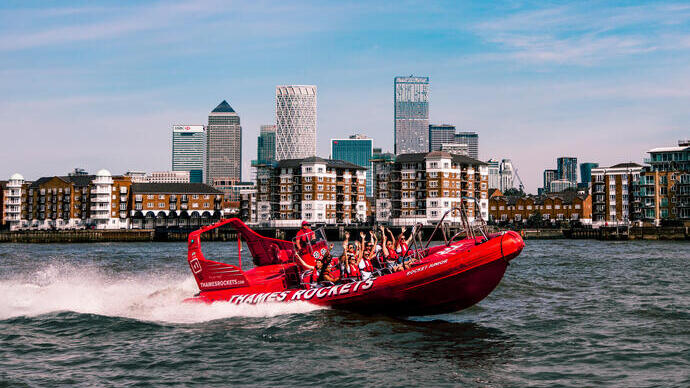 Pasajeros animando en una lancha rápida roja en el río Támesis frente a los rascacielos de Canary Wharf