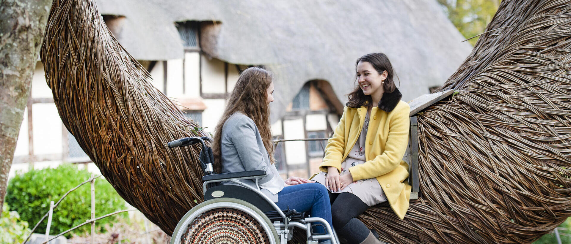 Wheelchair user and friend sat beside a wooden sculpture
