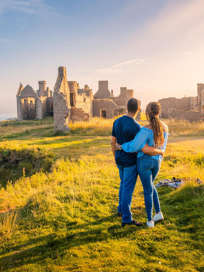 A couple enjoying the views of a castle remains at golden hour.
