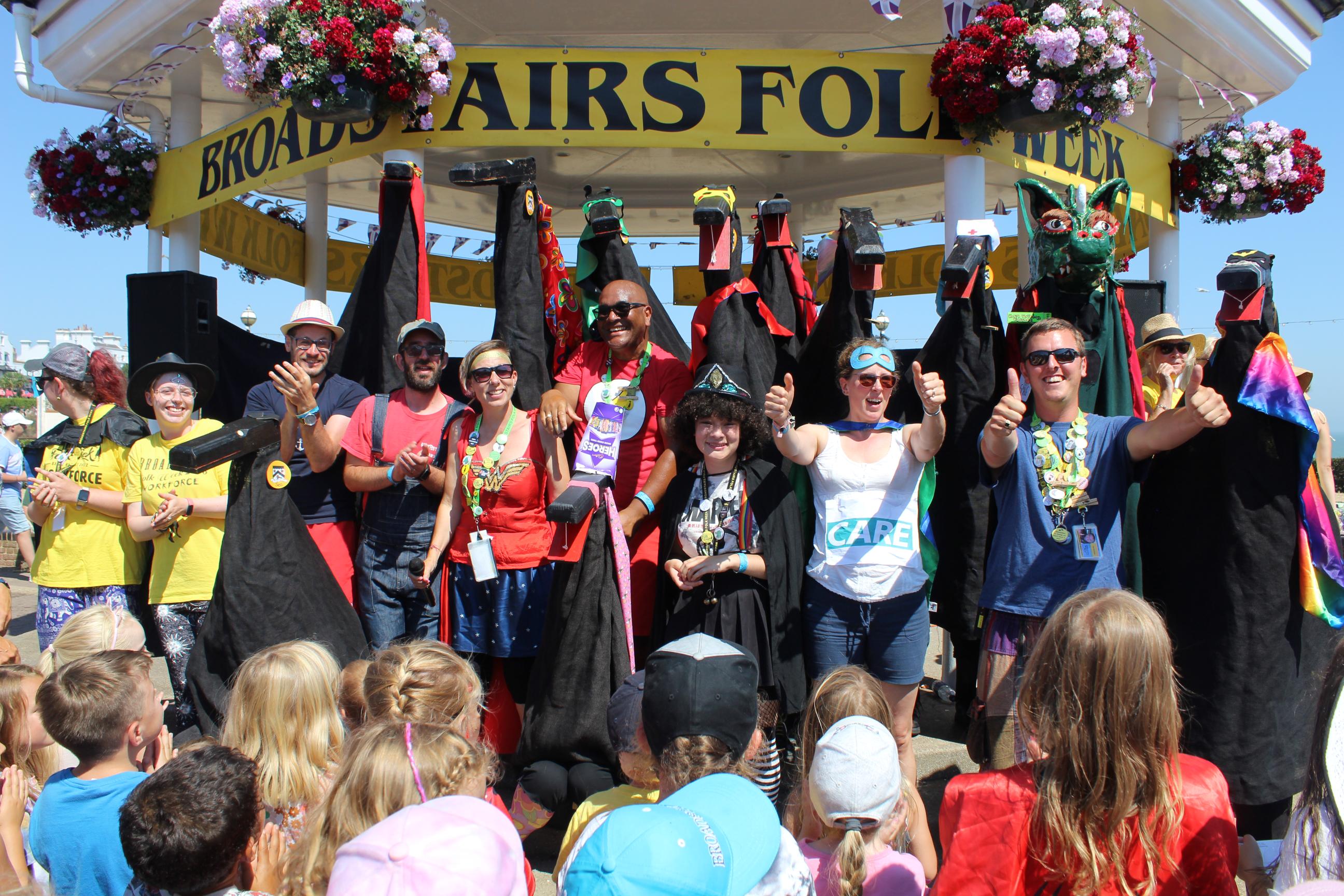 Crowd looking at people posing under a bandstand, with a banner reading: Broadstairs Folk Week