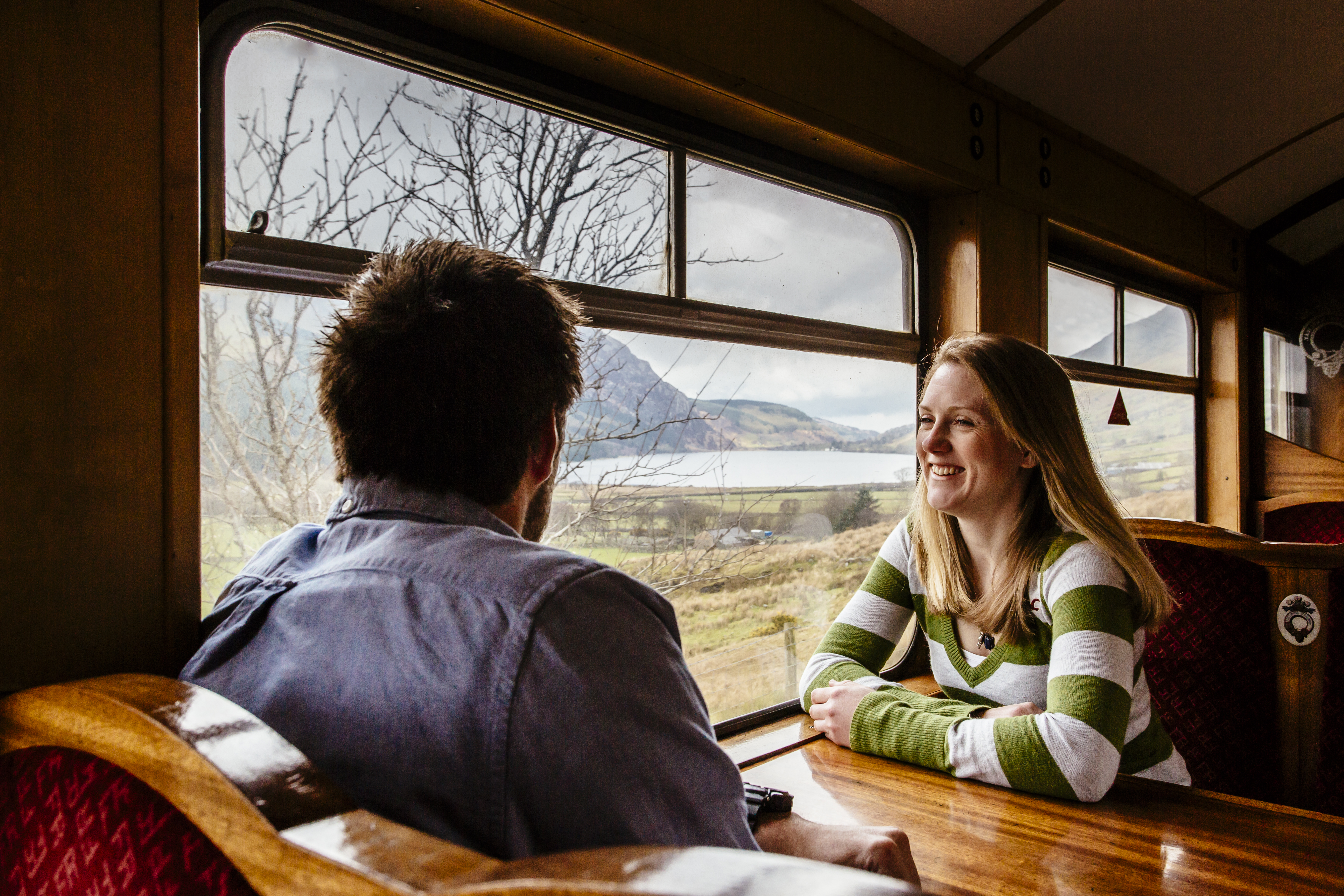 Couple sat at a table inside on a train passing through a mountainous landscape