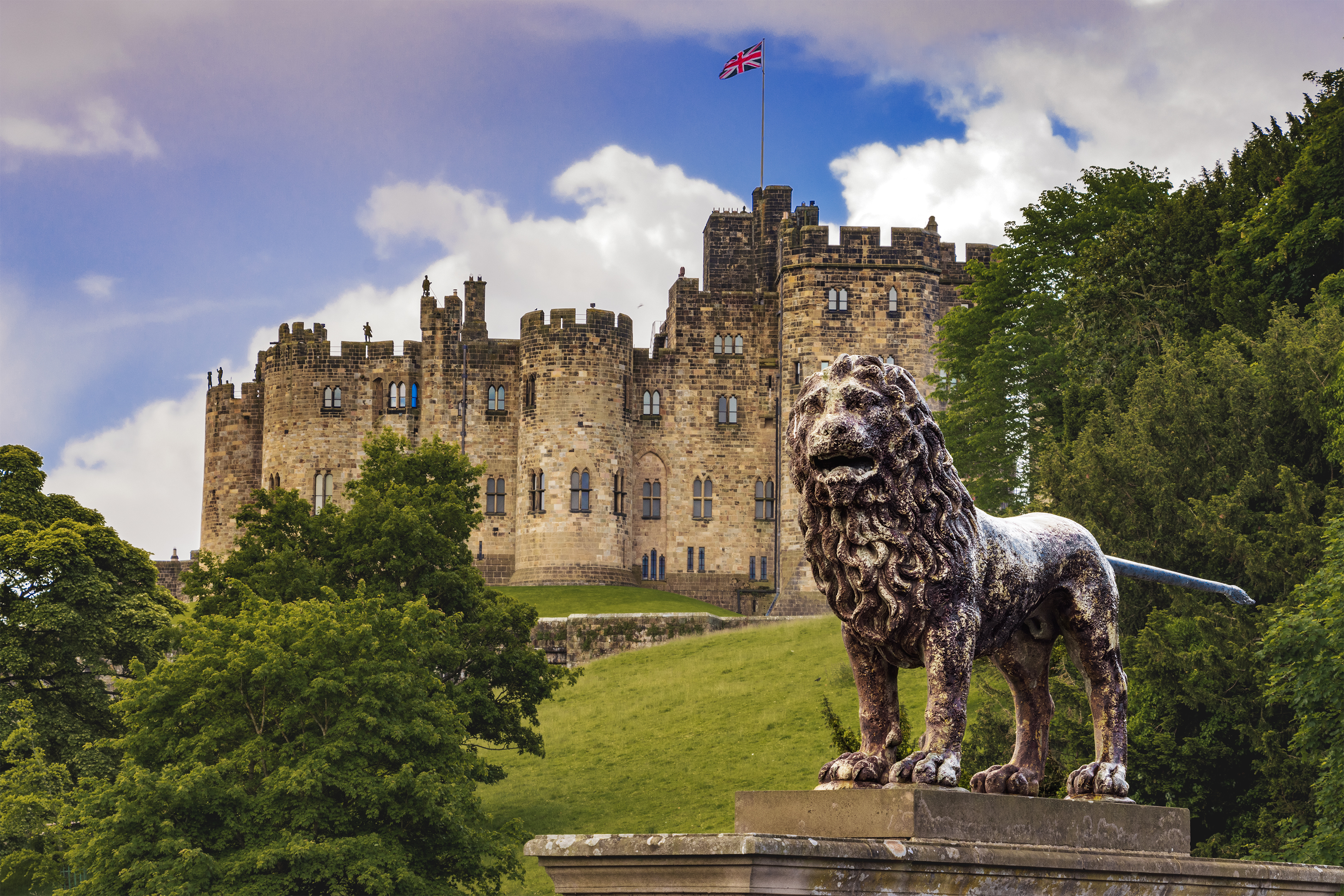 An historic castle with a UK flag at full mast and with a lion statue out the front.