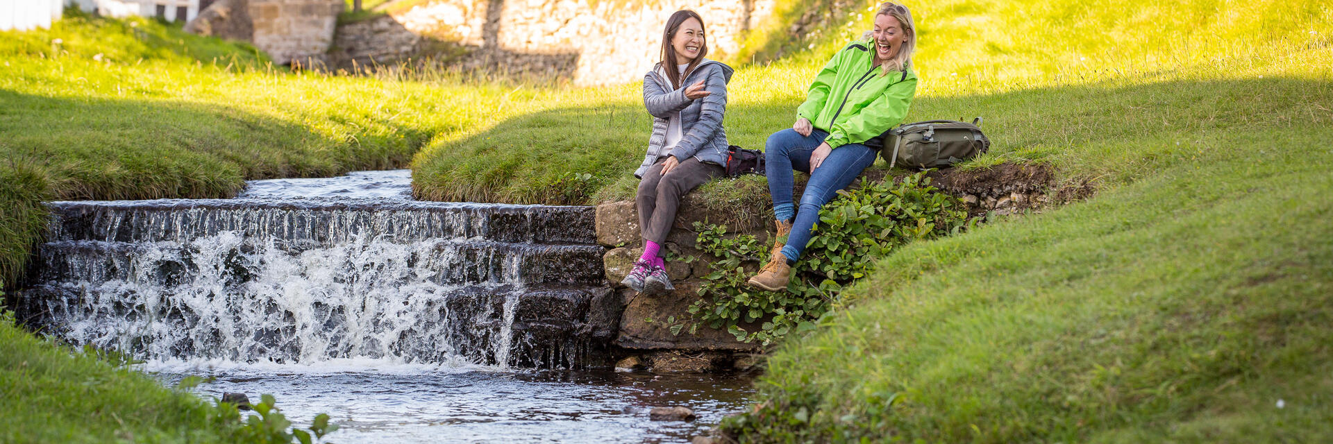 Two women sat on the banks of a stream, in a village
