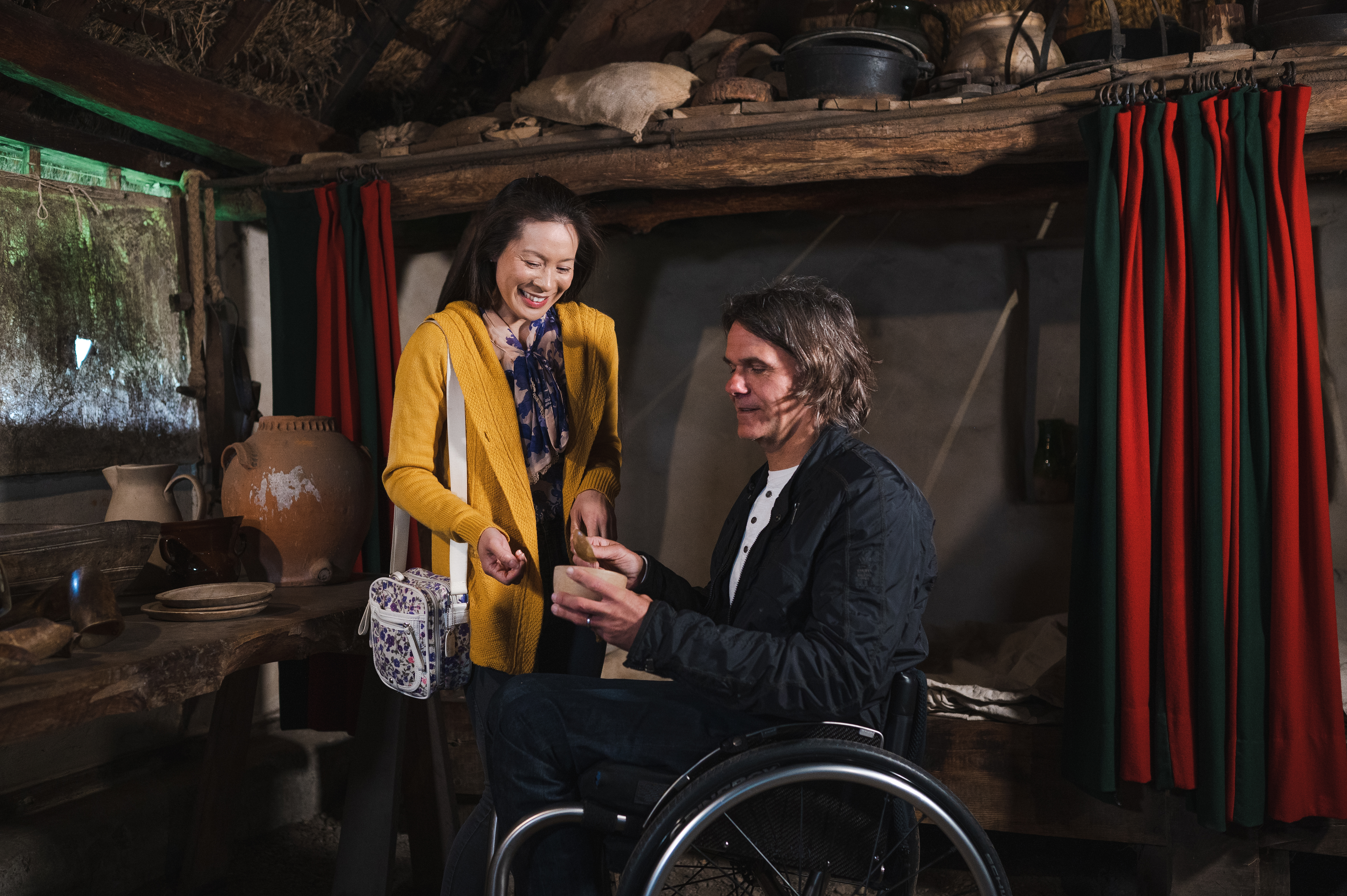 Man and woman, inside a recreated 15th century cottage looking at domestic utensils, man in a wheelchair