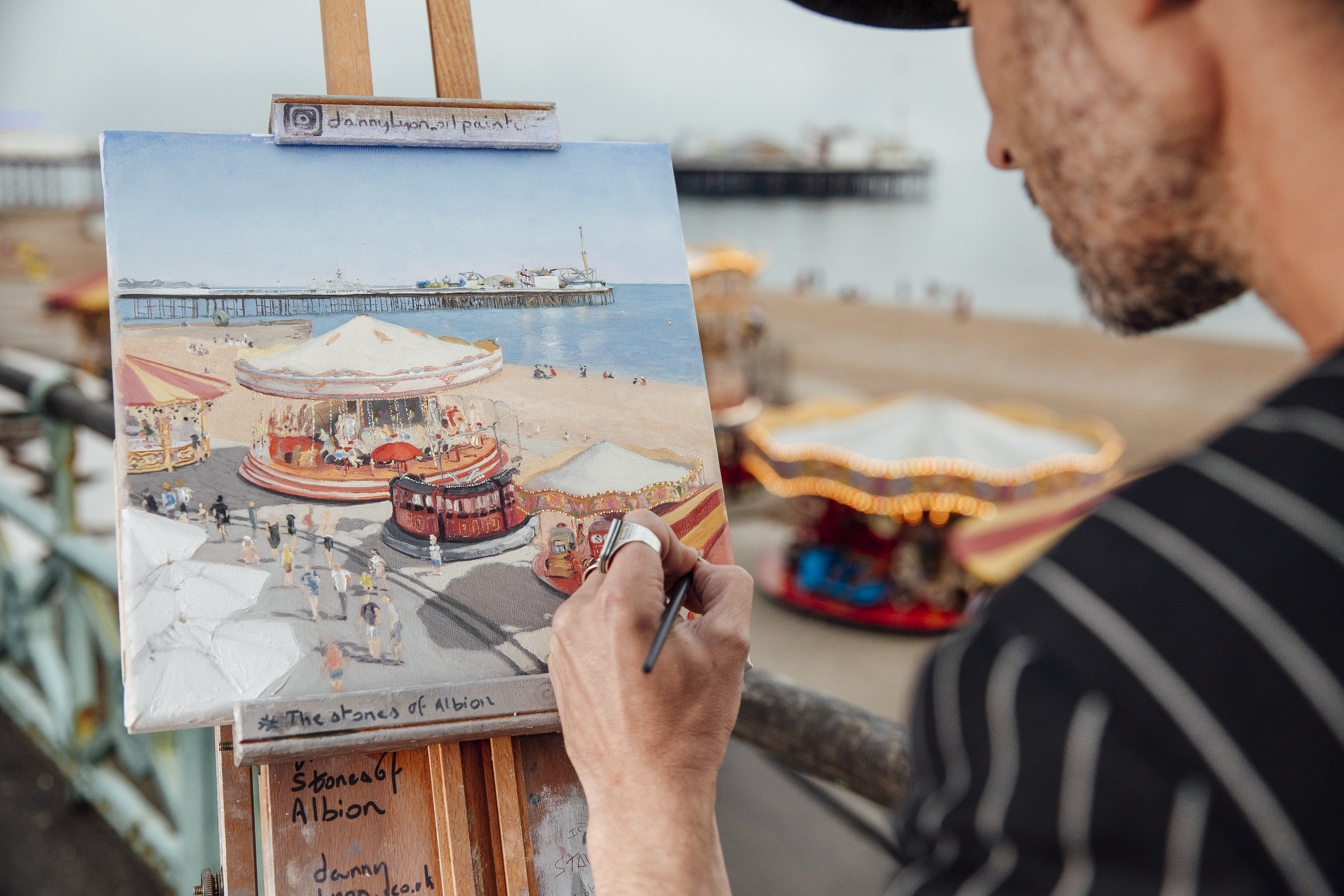 Artist doing a painting on an easel of the beach and funfair by the sea