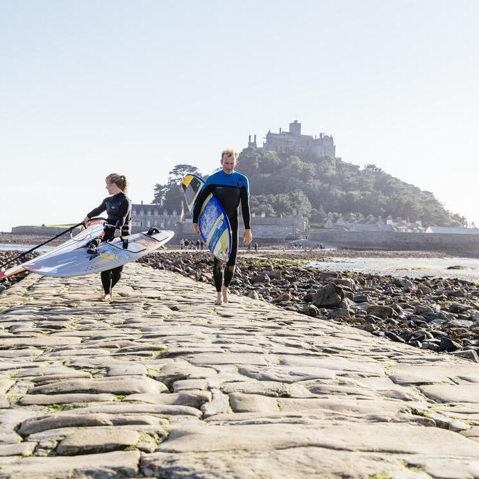 Windsurfers walking on a stone causeway that links an island to the mainland
