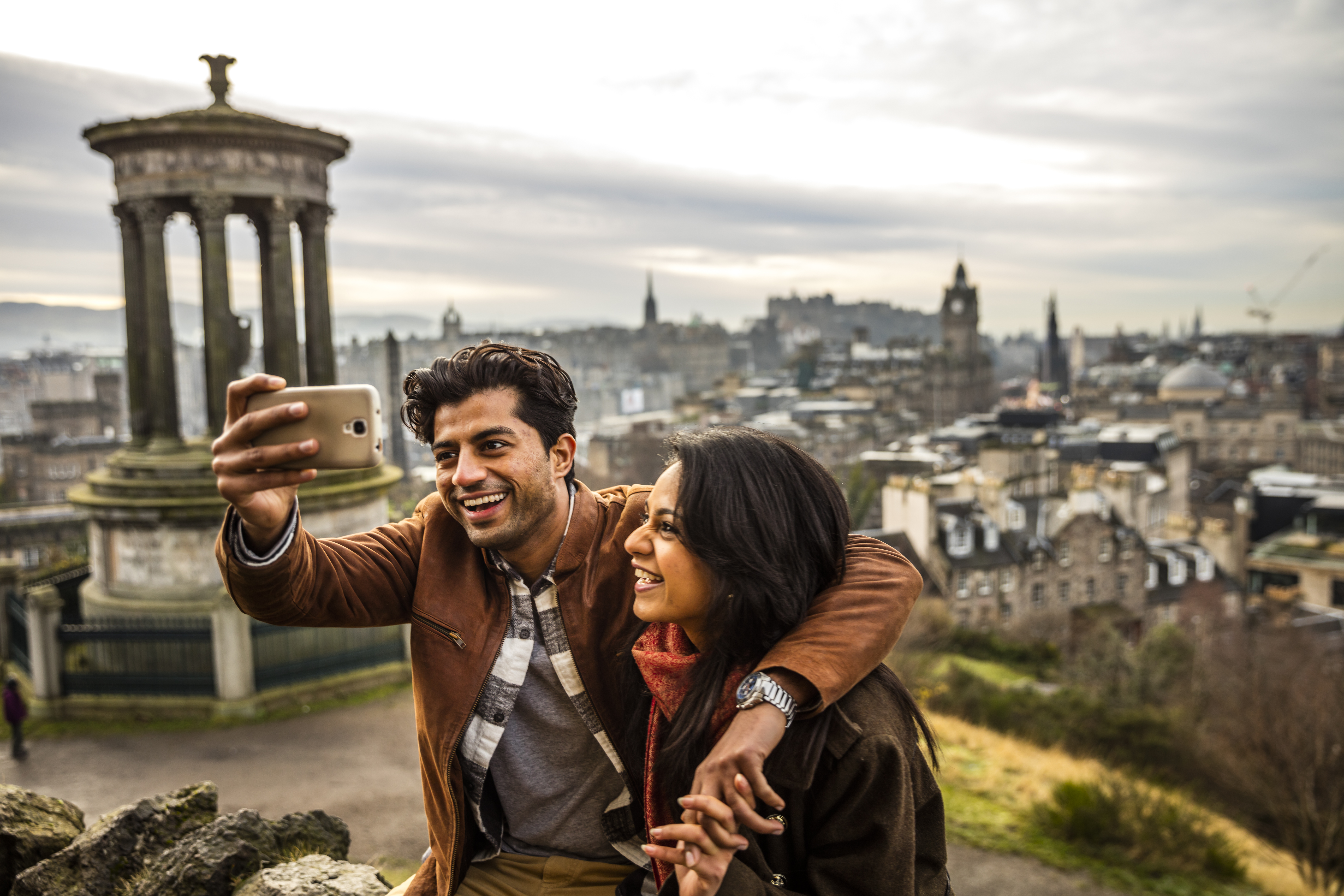 زوجان يلتقطان صورة سيلفي بهاتف محمول مع مدينة في الخلفية