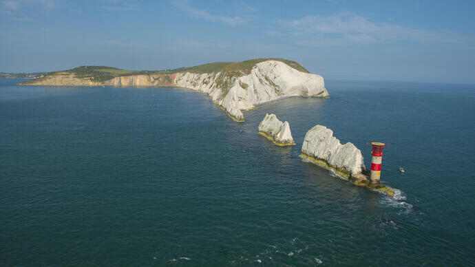 Tall chalk stacks in a row running from the cliffs of the mainland to a lighthouse