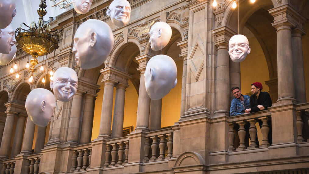 Two men looking at installation of suspended head sculptures